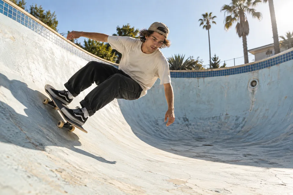 A young adult skateboarder in a sunlit empty swimming pool, candid documentary motion photograph