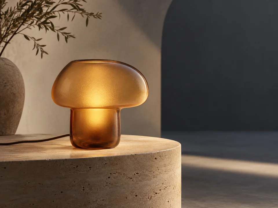 Amber glass lamp on a travertine plinth with warm light and cool shadows