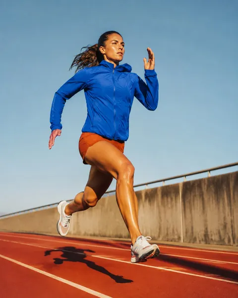 A sprinter in cobalt blue running across a sunlit vermilion track